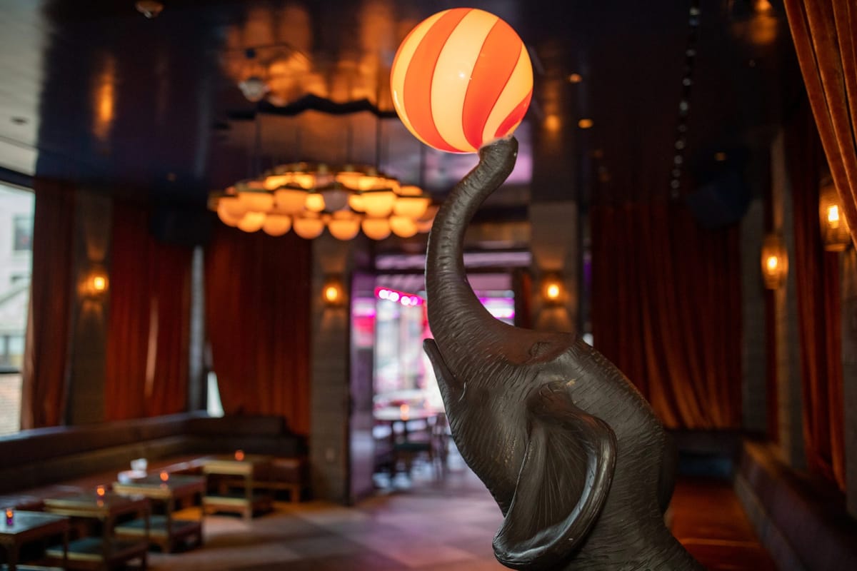 Bronze elephant statue balancing a red and white striped ball in a lounge with rust velvet curtains