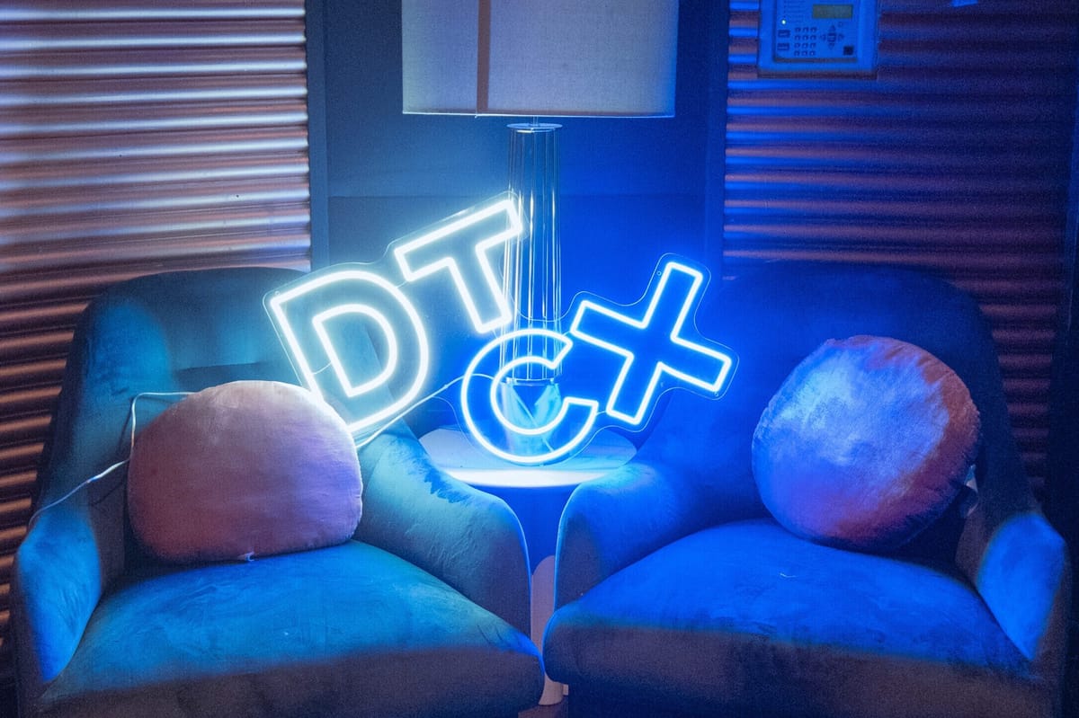 Neon DTCX sign glowing on a small table between two blue velvet armchairs with round cushions