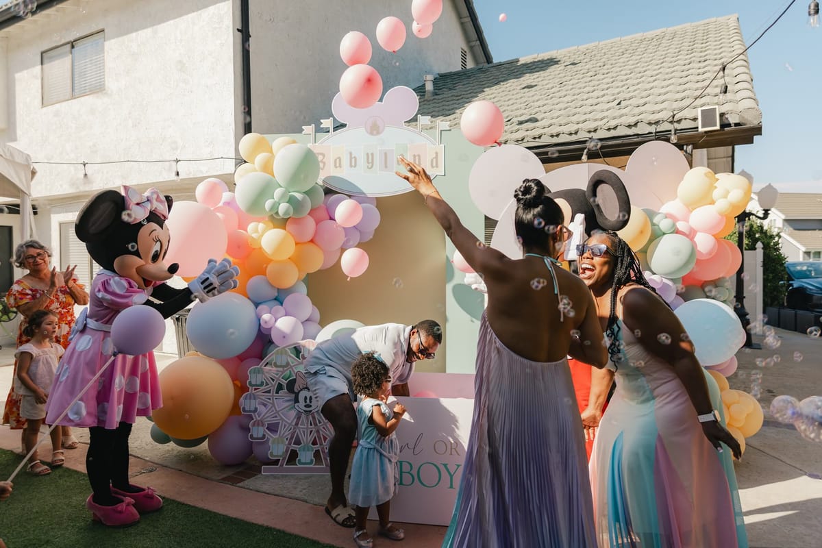 Pink balloons floating out of the reveal box in front of the Babyland arch as Minnie Mouse looks on
