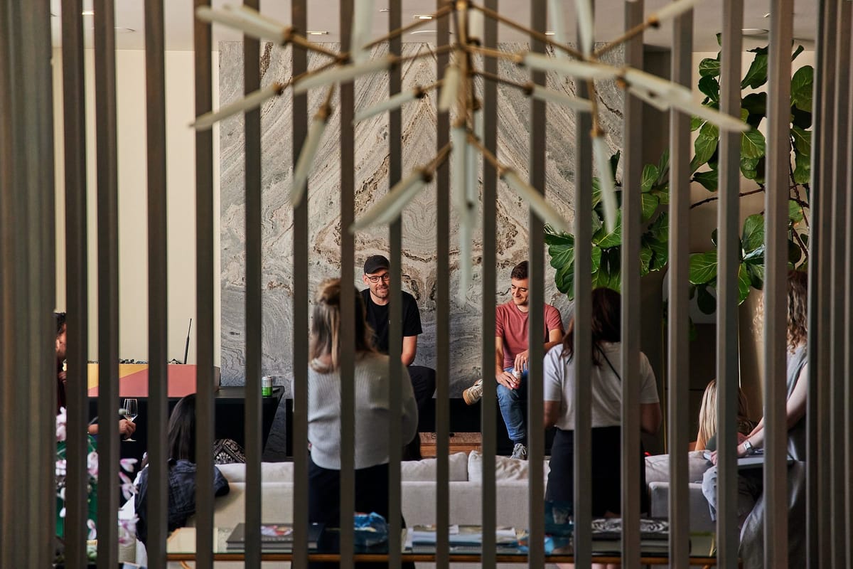 Guests on living room sofas during a session, seen through dark wooden slats, two men seated by a marble wall
