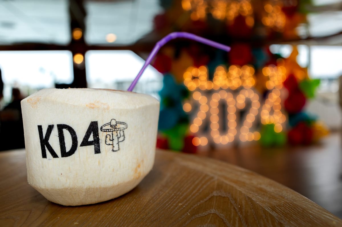 Coconut drink printed KD4 with a purple straw, lit Class of 2024 marquee letters blurred behind