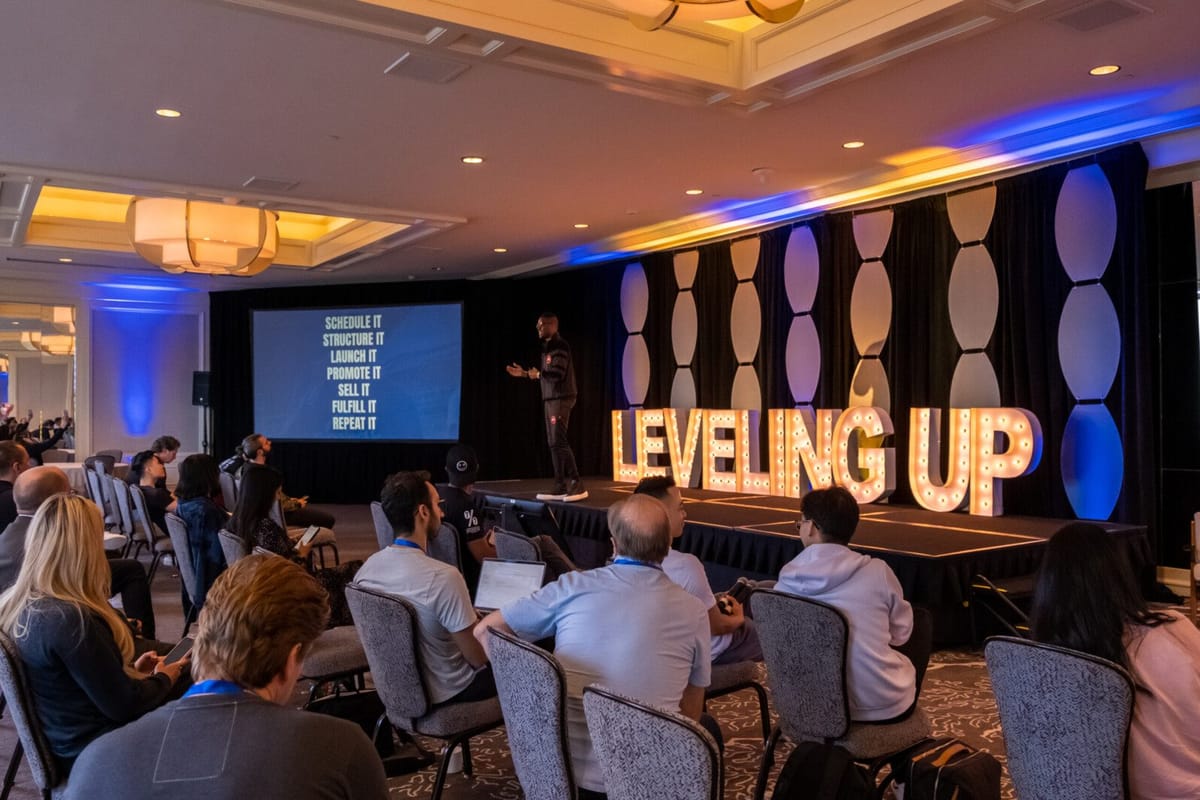 Audience watching a speaker beside a SCHEDULE IT, STRUCTURE IT slide and light-up LEVELING UP letters