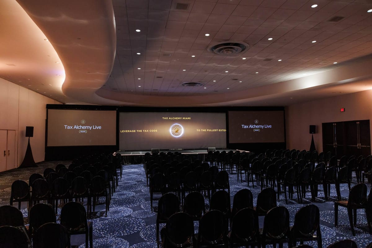 Dim conference room with rows of black chairs facing three screens under a curved, lit ceiling