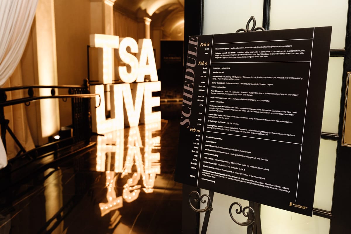 Lit TSA LIVE marquee letters reflected on a glossy floor beside a schedule board on an easel