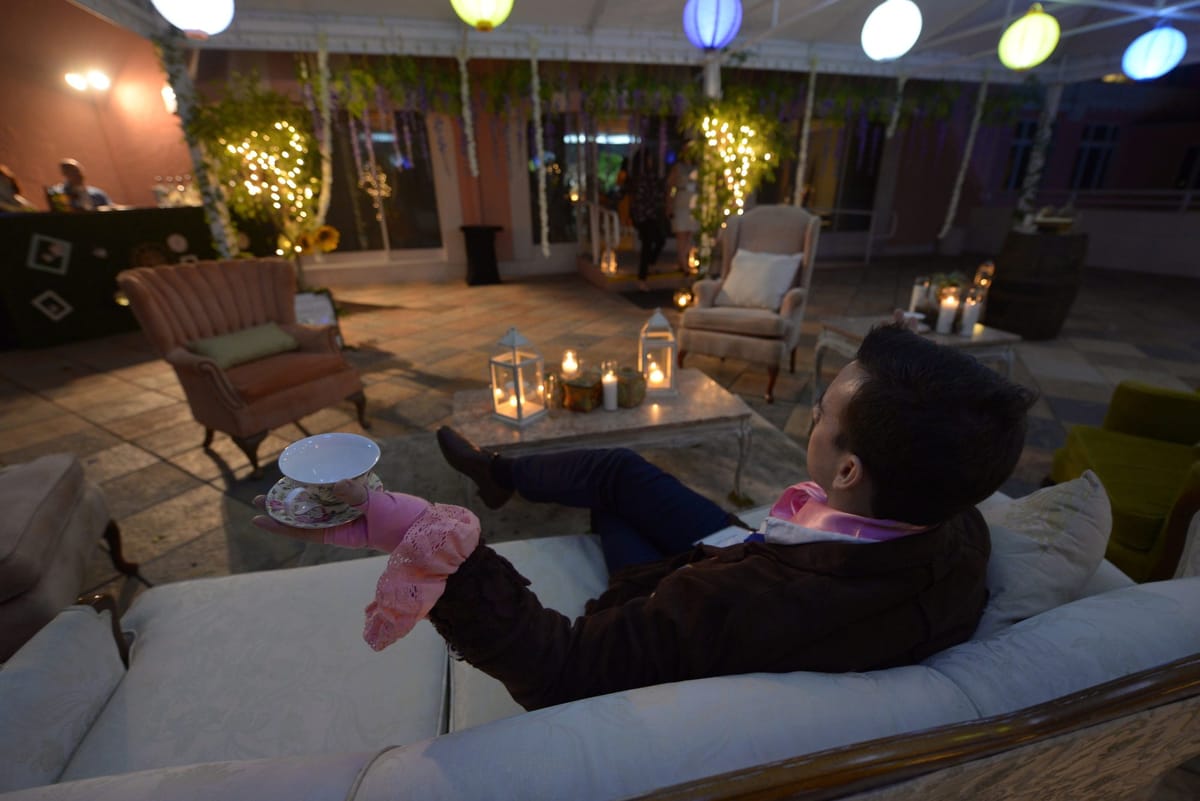 A guest reclining on a white sofa under colored paper lanterns, with armchairs and candle lanterns on a terrace