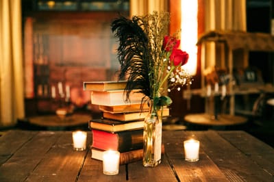 Stack of old books with a red rose and a black feather in a bottle among candles