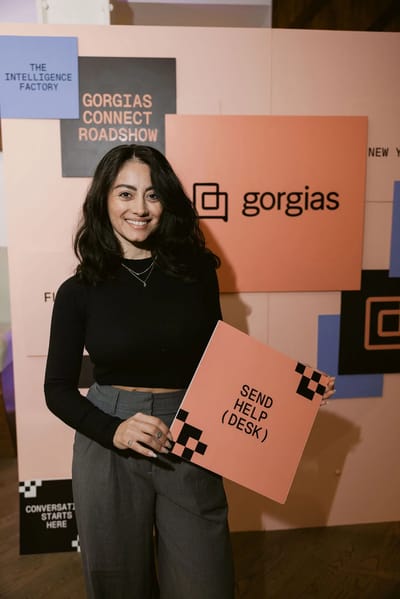 A guest holding a Send Help Desk sign in front of the Gorgias Connect colour-block wall