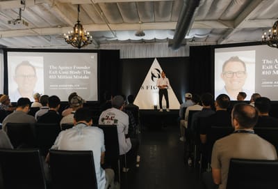 Full room watching a speaker between two screens showing an agency founder exit case study