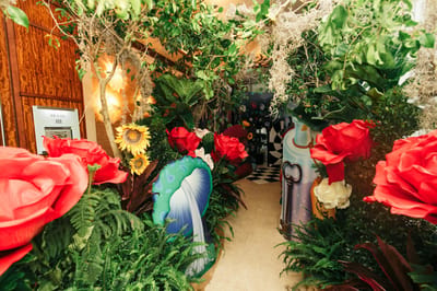 Oversized red roses, sunflowers, ferns and a painted mushroom cutout beside a wood-panelled doorway
