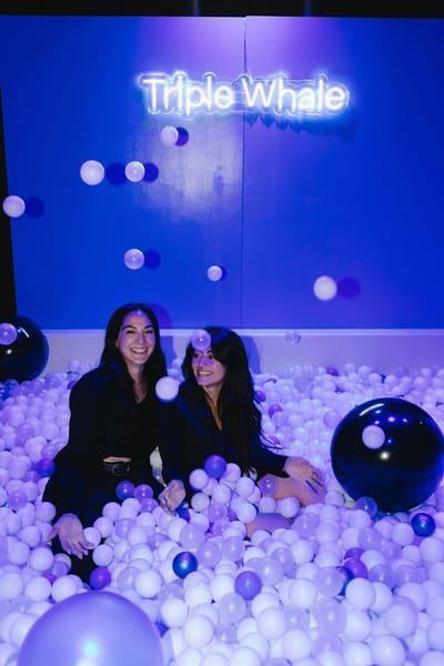 Two guests sitting in the ball pit under the Triple Whale neon and floating spheres