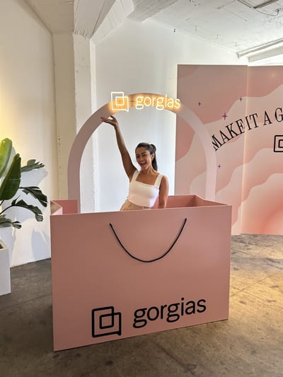 Samantha Pena waving from inside a giant pink Gorgias shopping bag under a neon Gorgias arch
