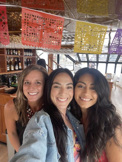 Samantha Pena and two women taking a selfie under strings of papel picado at a bar