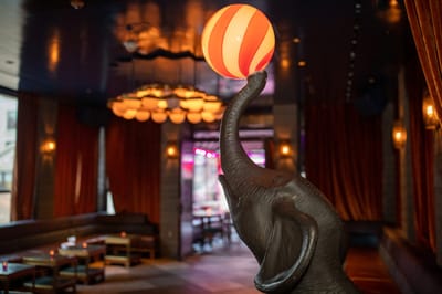 Bronze elephant statue balancing a red and white striped ball in a lounge with rust velvet curtains