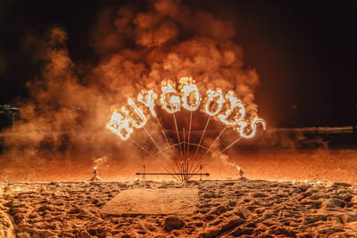 BUYGOODS spelled in burning fire letters on the beach at night, wrapped in smoke