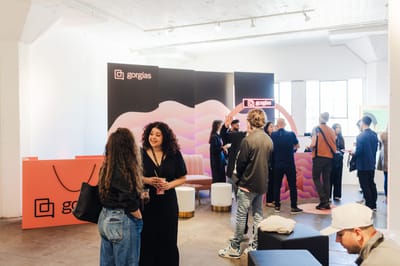 Guests talking at a Gorgias lounge with a coral shopping bag counter and a pink wave backdrop