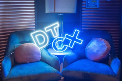 Neon DTCX sign glowing on a small table between two blue velvet armchairs with round cushions