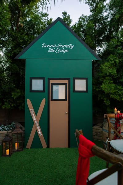 A green ski lodge facade built in a garden, skis crossed by the door