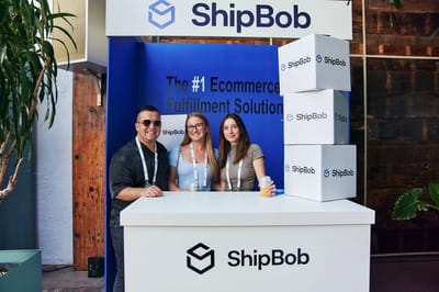 Three guests behind the ShipBob counter with stacked branded boxes