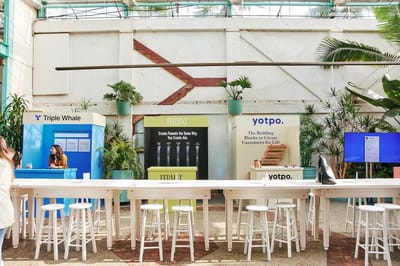 A row of sponsor stalls for Triple Whale, Fermat and Yotpo in a greenhouse venue