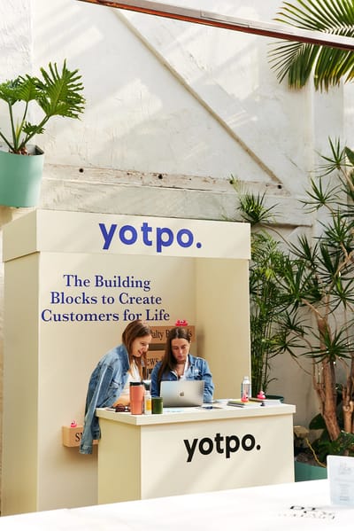 Two guests working at the Yotpo stall under the glasshouse roof