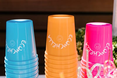 Stacks of blue, orange and pink cups printed ECOMCHELLA with smiley faces