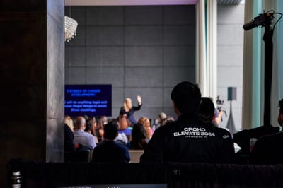 Audience watching a speaker beside a screen, with a guest in a CPOHQ Elevate 2024 jacket in the foreground
