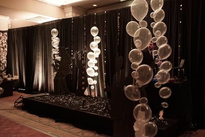 DJ stage with black drapes, clear balloon columns and black silhouettes of jazz musicians and a flapper, confetti on the floor