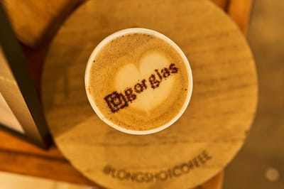 Latte with the Gorgias logo printed over heart foam art, on a wooden coaster marked @LONGSHOTCOFFEE