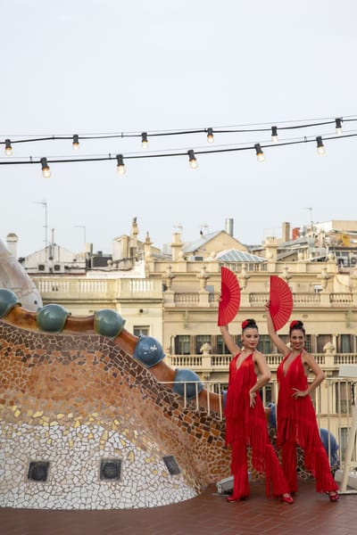 Two dancers in red holding red fans on the rooftop at dusk
