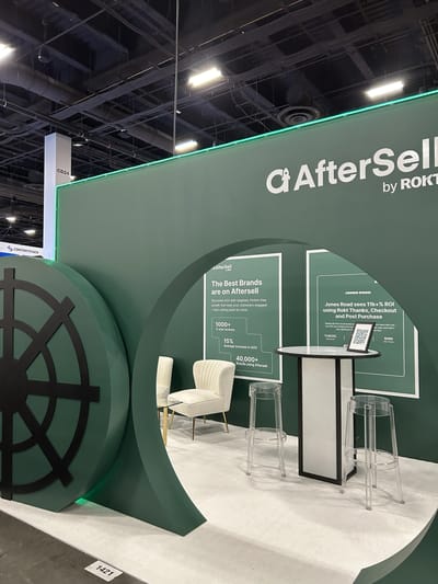 The green AfterSell booth wall with proof-point panels and a demo table
