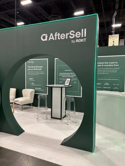 The green AfterSell by Rokt booth with a bank vault door