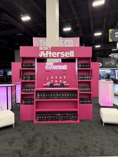 A hot pink Rokt AfterSell booth styled as retail shelving stocked with product