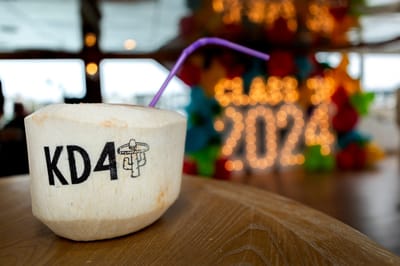 Coconut drink printed KD4 with a purple straw, lit Class of 2024 marquee letters blurred behind