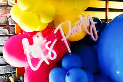White neon Let's Party sign set on a cluster of yellow, pink and blue balloons