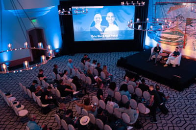 Audience in a patterned-carpet ballroom facing a stage under a screen reading Eric Siu & Neil Patel