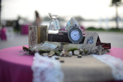 Small clock, a Drink Me bottle, a teacup and old books on a pink tablecloth with a lace runner