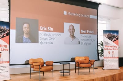 Stage screen showing Eric Siu of Single Grain and Neil Patel of Neil Patel Digital above two orange lounge chairs