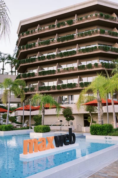 Orange and black maxweb letters standing in a hotel pool below balconies lined with plants
