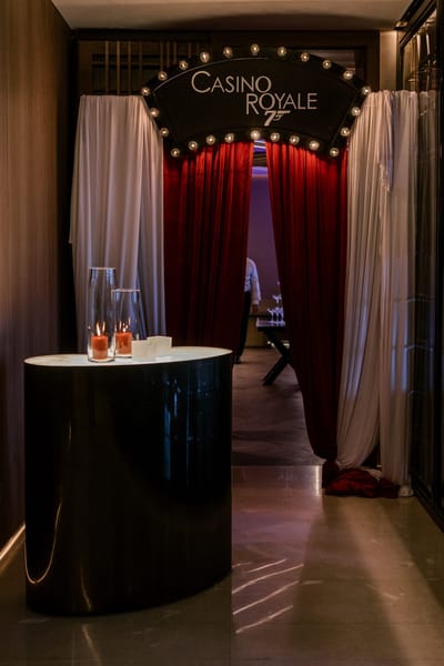 Lit CASINO ROYALE marquee sign above red velvet curtains and white drapes, with candles on a side table