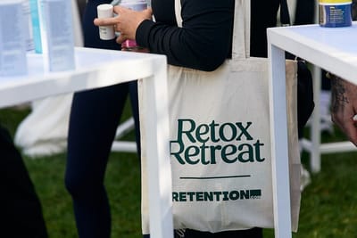 Canvas tote bag printed with Retox Retreat and Retention, carried between white tables on a lawn
