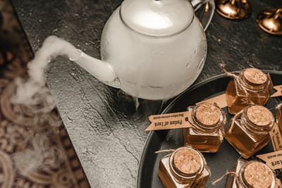 Glass teapot trailing fog beside corked Potion of Luck jars with brown paper tags on a dark tray