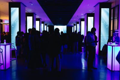 Guests in silhouette between tall pillars fitted with glowing LED screens, with bar tables lit from inside
