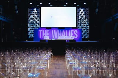 Rows of clear chairs facing a stage with white sofas, THE WHALIES letters and a Triple Whale screen