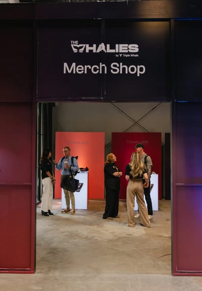 The Whalies Merch Shop entrance lit in red with guests browsing plinths