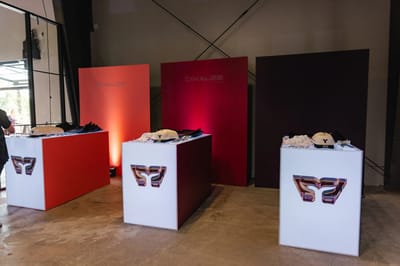 Three lit plinths displaying caps and merch against red and black panels
