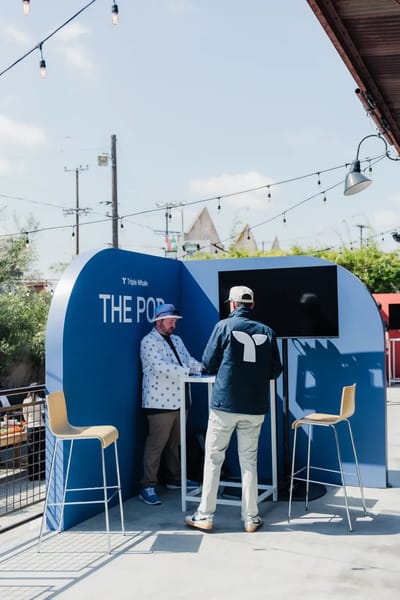 A blue Triple Whale demo pod with a screen, stools and guests mid-conversation