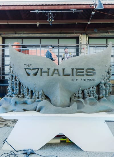 A whale tail sculpted from sand with The Whalies logo carved into it