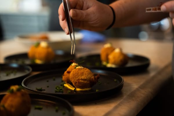 A chef using tweezers to garnish fried bites on black plates