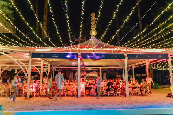Guests dining in a white tent on the sand under fairy lights radiating overhead