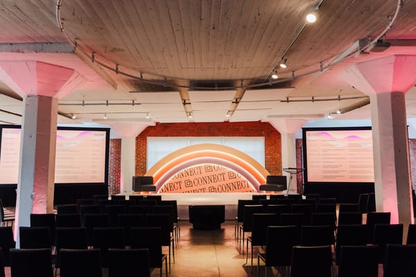 Main room with rows of black chairs facing an arch-shaped rainbow Connect backdrop between two agenda screens